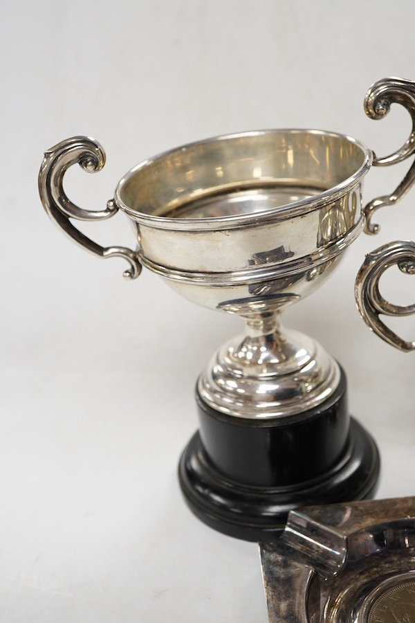 A pair of George V small silver two handled trophy cups by J W Tiptaft & Son Ltd, Birmingham, 1933, height 10cm, one with plinth, together with a George V silver ashtray with inset coin base.